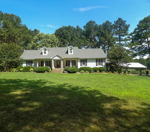 Front elevation of the Waterside Lodging farmhouse with wraparound porch and gardens